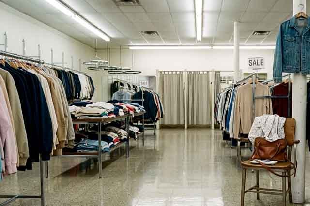 Tienda de ropa de los 80 con luz de fluorescentes, suelo brillante y perchas metálicas, en una escena poética y nostálgica.