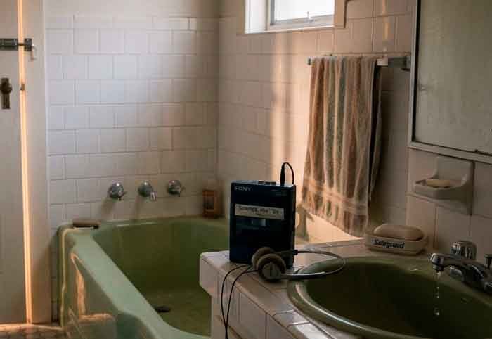 Baño tenue y silencioso con walkman y grifo goteando, en una escena poética y protegida.