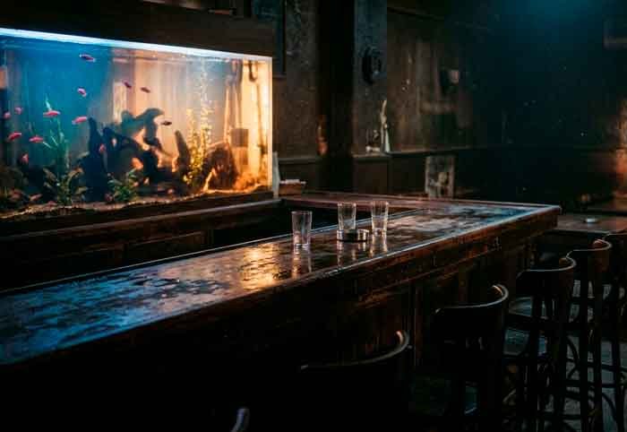 Bar antiguo iluminado como si estuviera bajo el agua, con una pecera gigante proyectando reflejos ondulantes