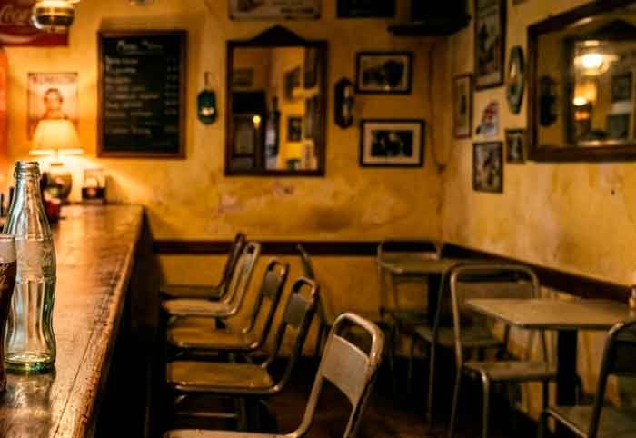 Bar antiguo y vacío con dos bebidas sobre una mesa y luz cálida, en una escena íntima y silenciosa.