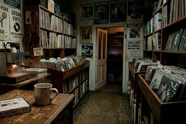 Tienda de discos de los 80 con carteles gastados, cinta fotocopiada y olor a vinilo, en una escena poética y minimalista.