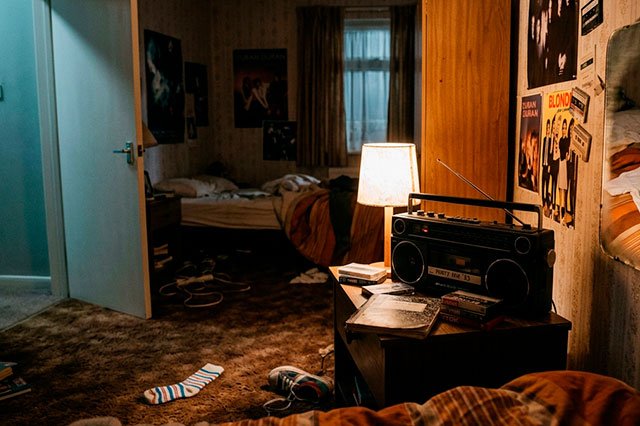 Habitación ochentera vacía con un radiocasete, un espejo, ropa preparada y un calcetín infantil en el suelo, iluminada con luz suave.