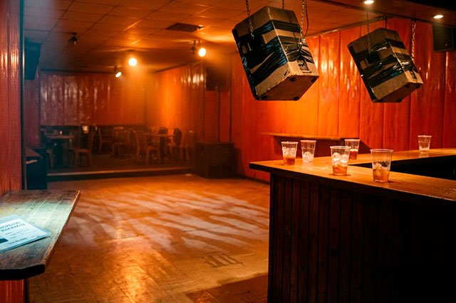 Discoteca poética con luz naranja, pista brillante, vasos abandonados y un carnet genérico iluminado en penumbra.