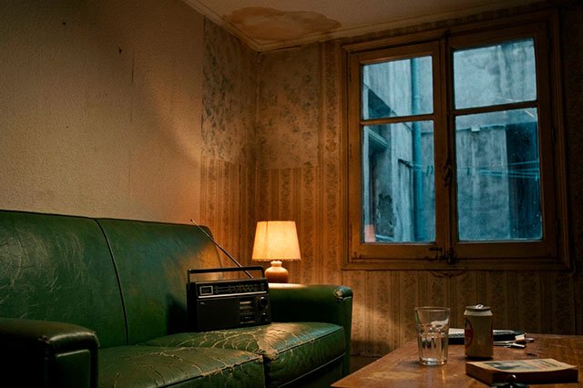 Sofá de escay verde en un salón nocturno con una radio encendida y luz cálida en un piso antiguo de Lavapiés